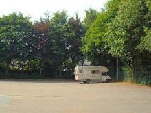 Wohnmobil auf Parkplatz, umgeben von Bäumen.