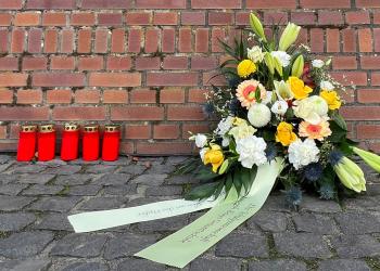 Ein Blumengesteck und fünf Grabkerzen vor einer Backsteinmauer am Synagogenplatz in Kleve