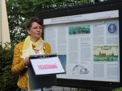 Gästeführerin zeigt historische Abbildung vor dem Schaukasten an der Schwanenburg