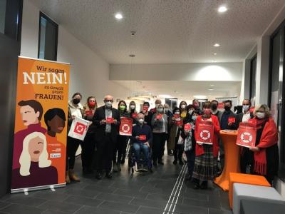 Eine Gruppe von Menschen steht mit roten Taschen, Postkarten und Plakaten mit dem Logo des Runden Tisches neben einem Banner auf dem steht "Wir sagen Nein" zu Gewalt gegen Frauen"