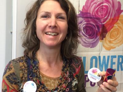 Eine Frau hält lächelnd einen Sticker mit der Aufschrift "Frauenrechte stärken" in die Kamera 
