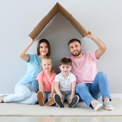 Familie unter einem schützenden Dach aus Pappe als Symbol