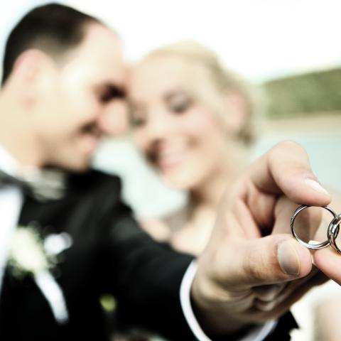 Ein Brautpaar hält gemeinsam einen Ehering in die Kamera