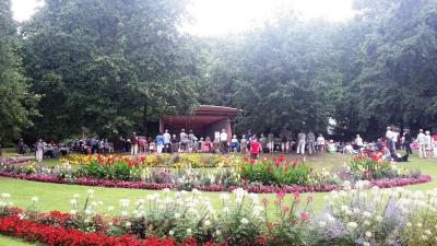 Bunte Blumen im sommerlichen Forstgarten, im Hintergrund sind Menschen vor der Konzertmuschel versammelt.