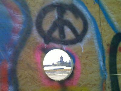 Eine Fotografie zeigt die Schwanenburg durch eine Loch in einer Wand, auf der darüber ein Peace-Zeichen gemalt ist 
