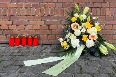 Ein Blumengesteck und fünf Grabkerzen vor einer Backsteinmauer am Synagogenplatz in Kleve
