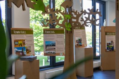 Ein Bild der Ausstellung nachhaltiges Bauen vor dem Ratssaal. Zu sehen sind Erklärungsschilder und Bäume aus Pappe.